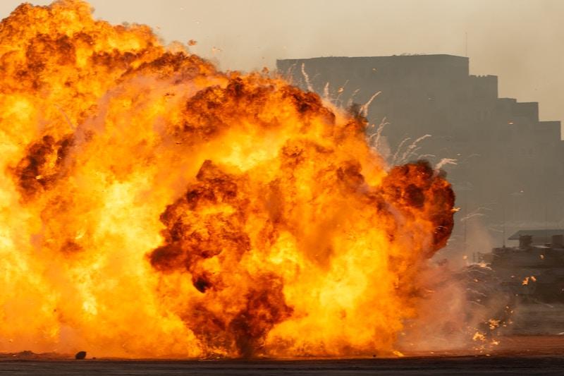 Großer Feuerball vermutlich nach einer Explosion, im HIntergrund der Umriss eines Gebäudes.